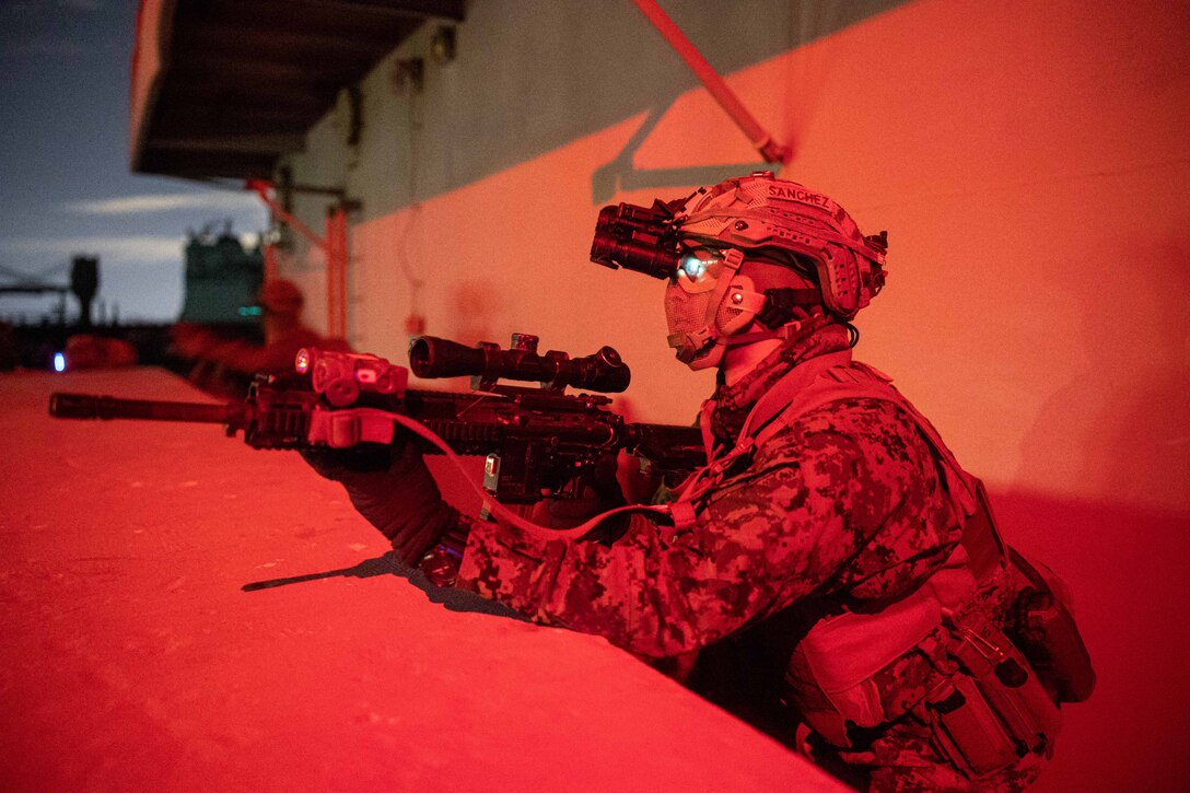 A Marine is shown holding a weapon while looking into the distance.