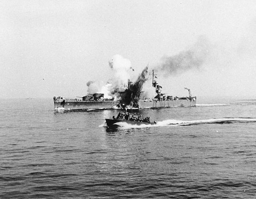 Smoke pours from a large ship as a smaller boat passes in the foreground.