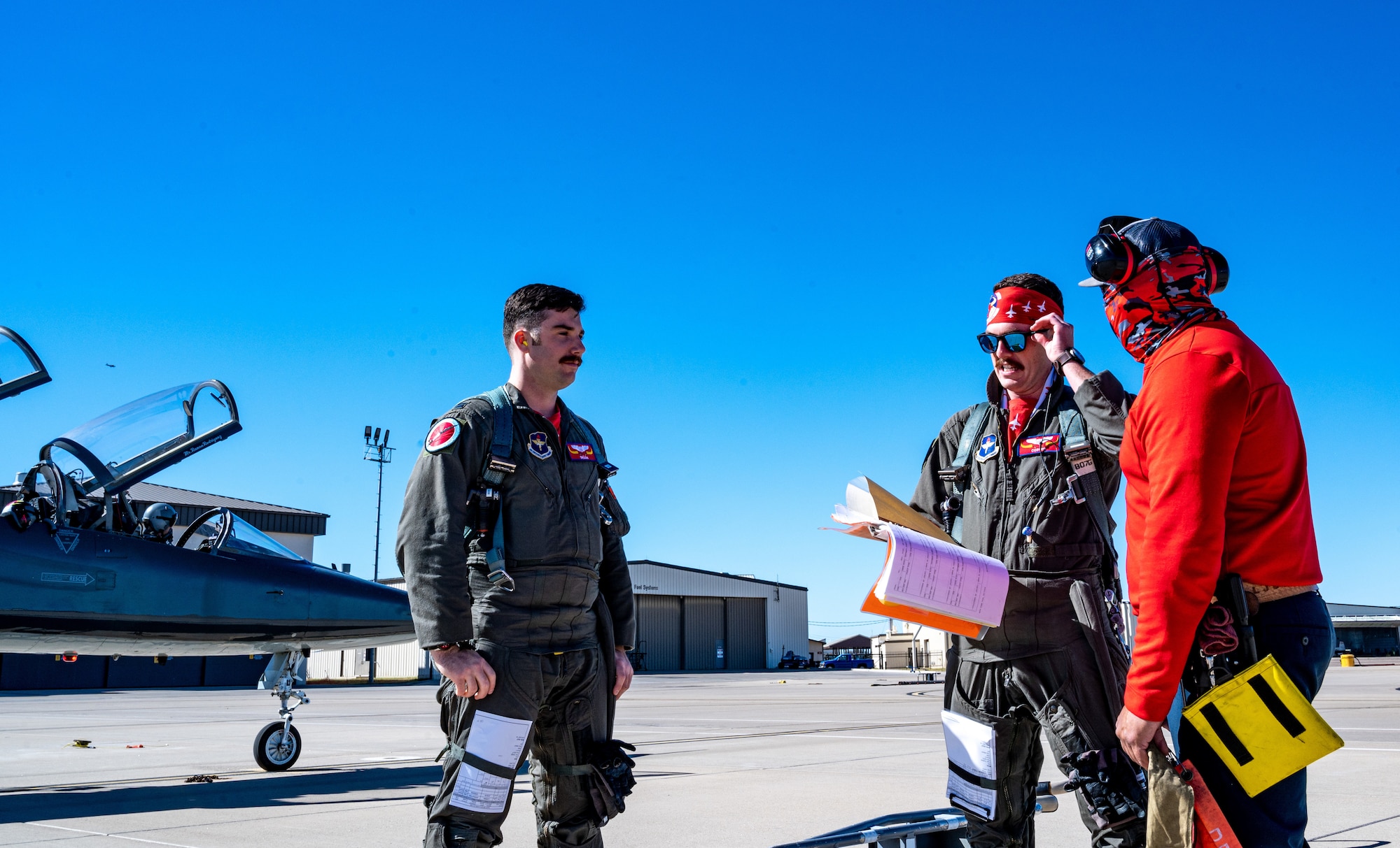 U.S. Air Force Capt. Garrett Green (left), 87th Flying Training Squadron instructor pilot, and Capt. Tyler Coplen (middle),  47th STUS instructor pilot, communicate concerns about aircraft with a local maintainer on Jan. 13, 2023, at Laughlin Air Force Base, Texas. In case of any issue where an aircraft cannot fly, the scheduling team keep aircraft in reserve, so training won't be delayed. (U.S. Air Force photo by Senior Airman David Phaff)
