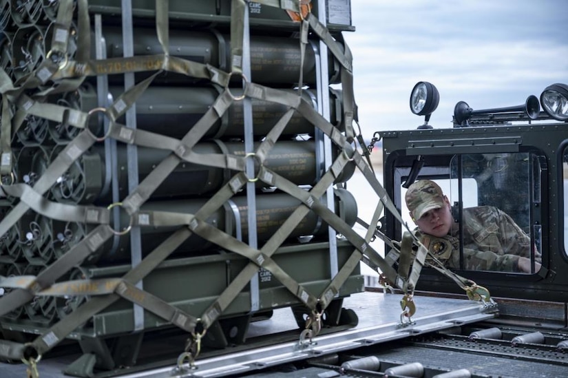 A man in a truck maneuvers a pallet of munitions.