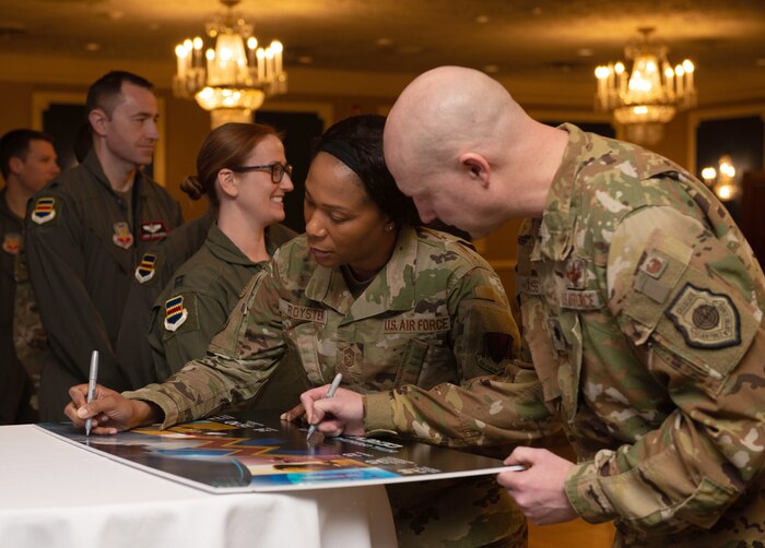 A woman and man wearing camouflage uniforms sign a poster