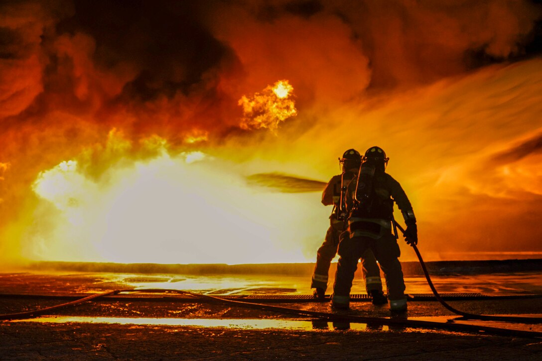 Two Marines use a hose to put out a fire.