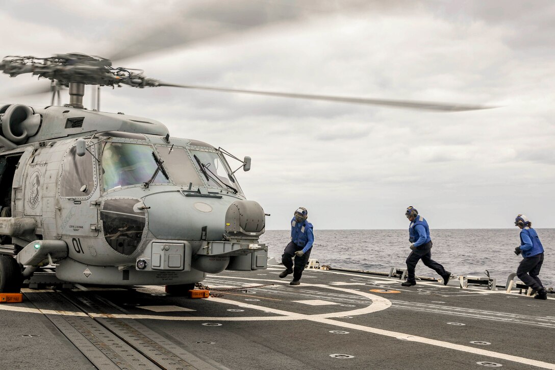 Three sailors run near a helicopter aboard a ship at sea.