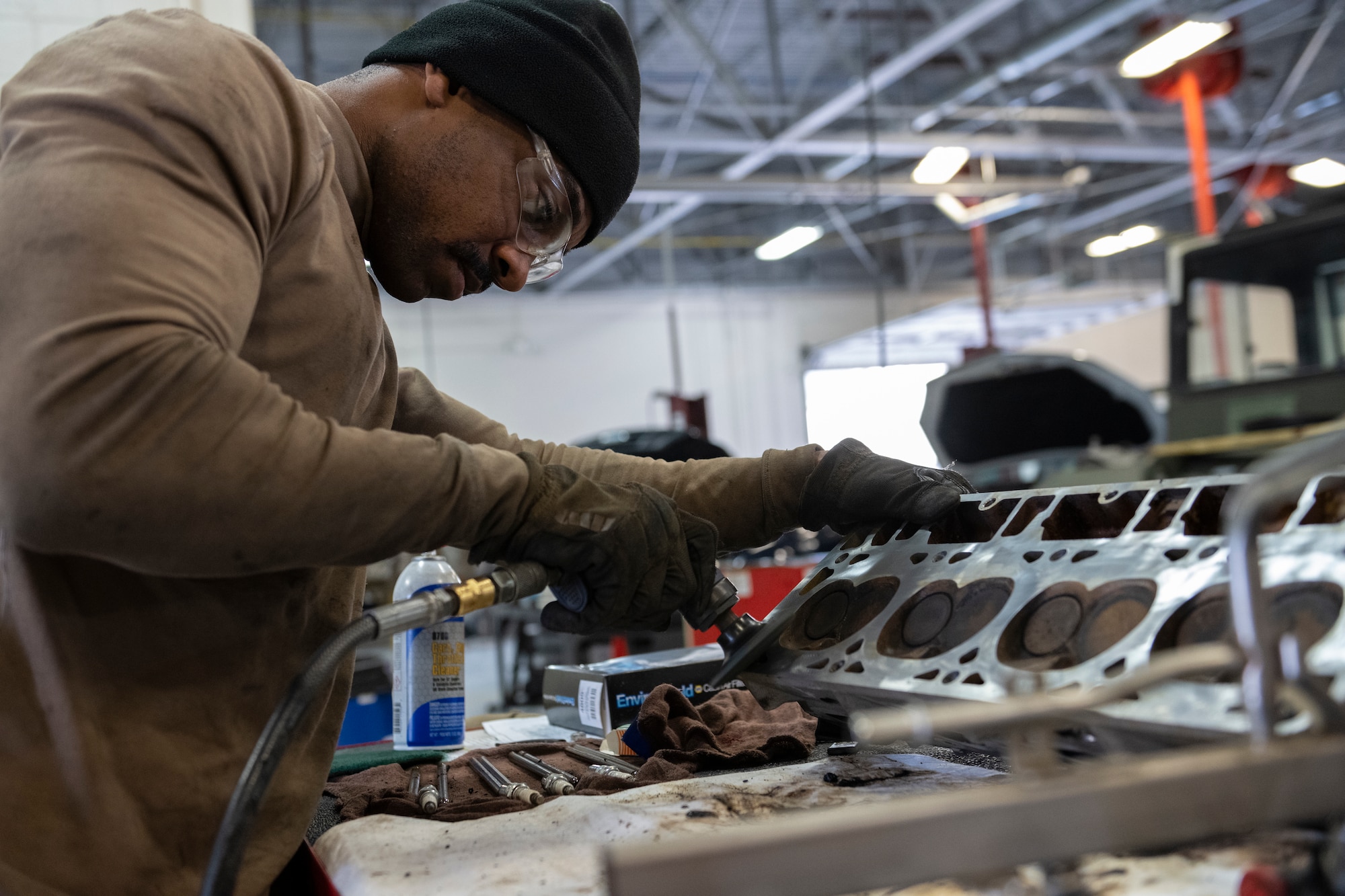 A photo of an Airman sanding a cylinder head with a handheld power drill/sander.