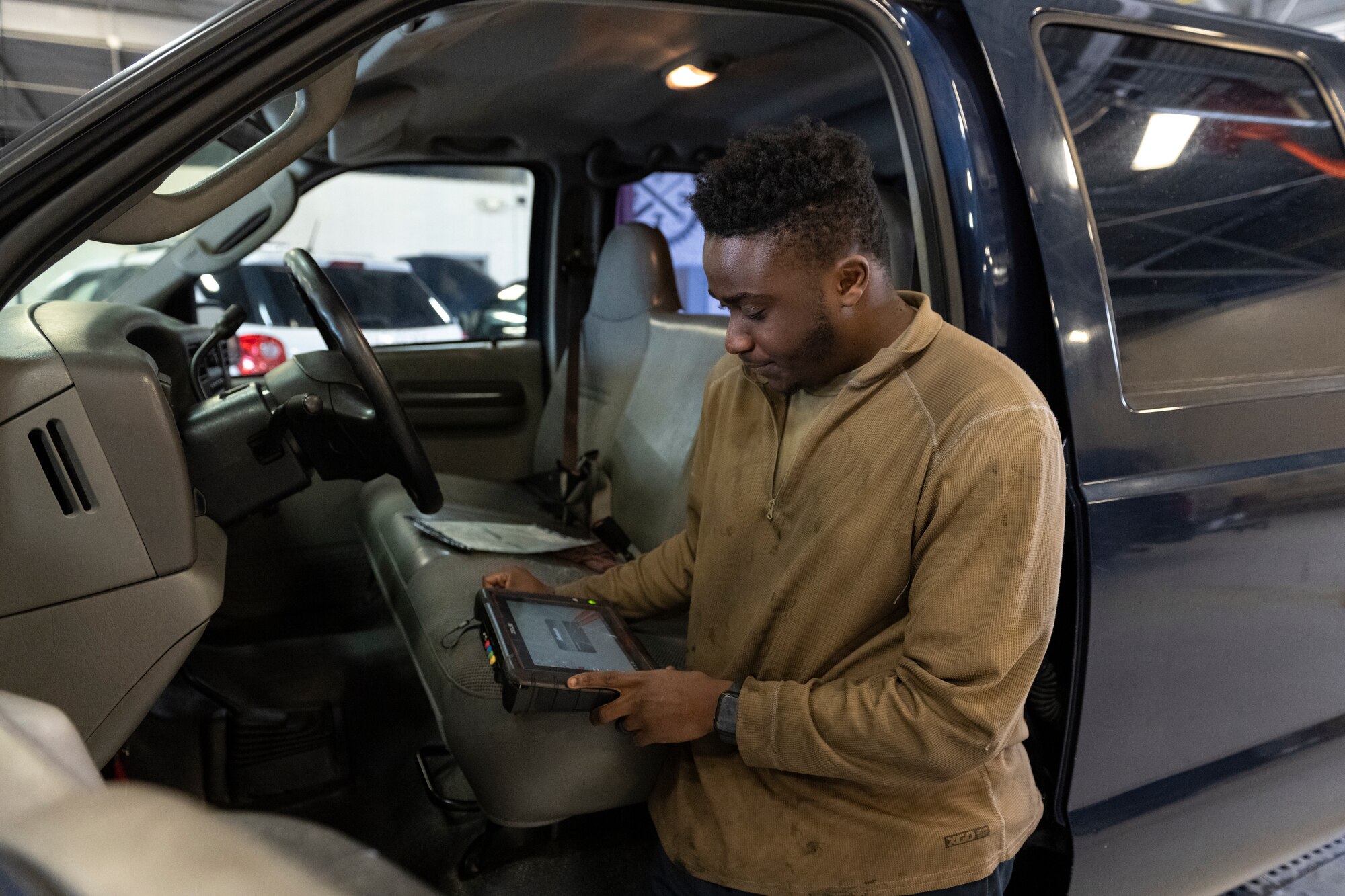 A photo of an Airman leaning against a truck, holding an iPad of sorts looking at it.
