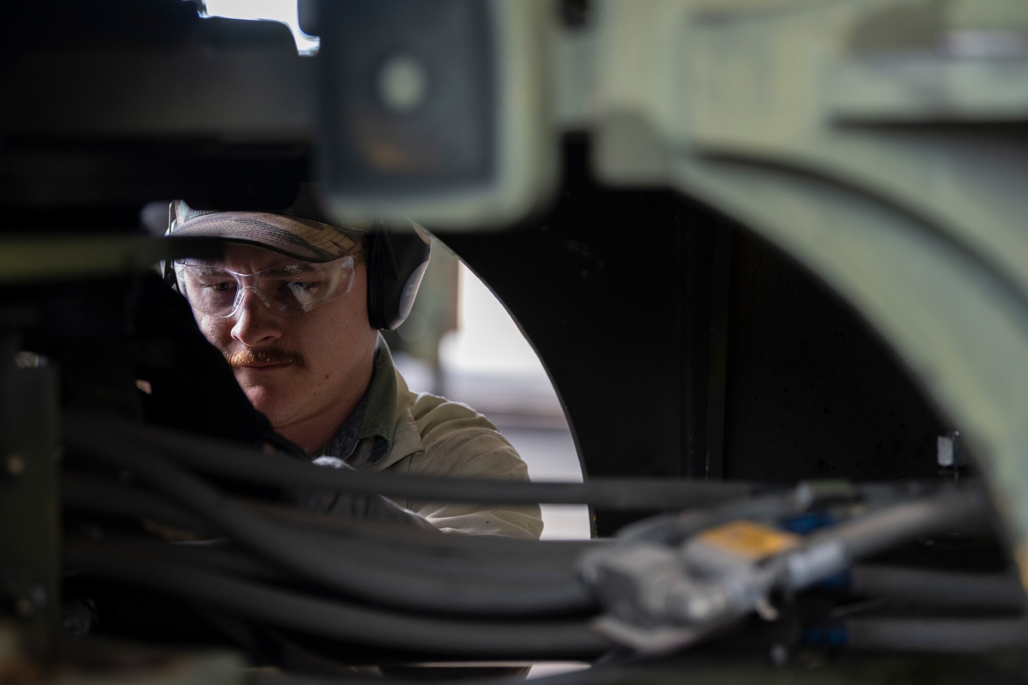 A photo of a civilian crouched on the ground on the other side of a forklift and the photo is taken through an opening.