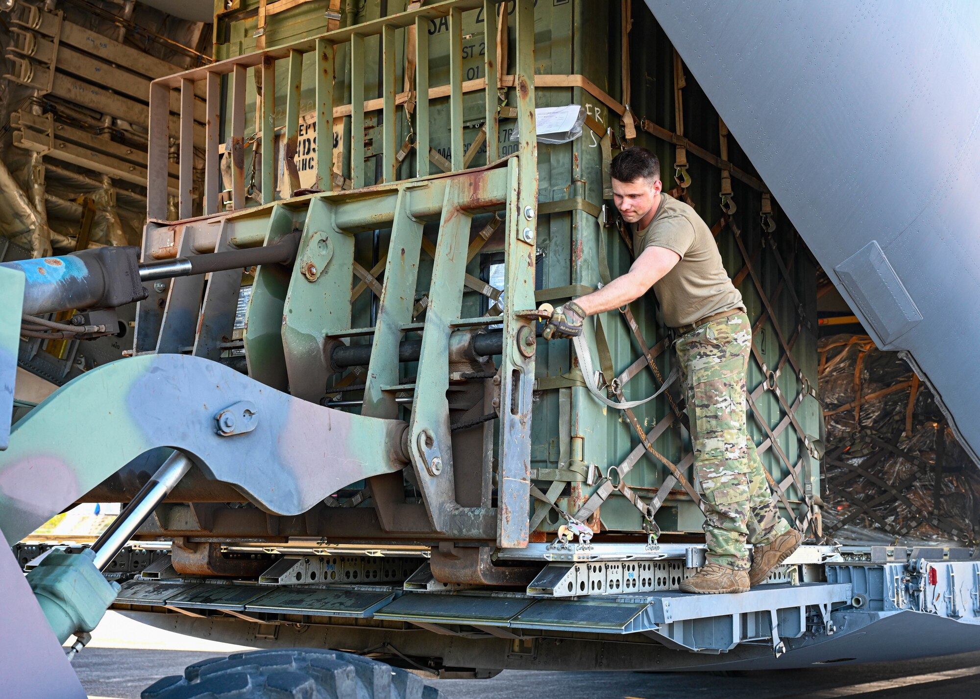 Senior Airman Andrew Girard, 535th Airlift Squadron C-17 Globemaster III loadmaster, secures a palette to a forklift at Hilo, Hawaii, Jan. 10, 2022. Girard offloads cargo in support of the 25th Infantry Division’s gunnery sustainment exercise which simultaneously maintains Soldier’s weapons proficiency and strengthens air, land and sea deployment capabilities within the Indo-Pacific. (U.S. Air Force photo by Senior Airman Zoie Cox)