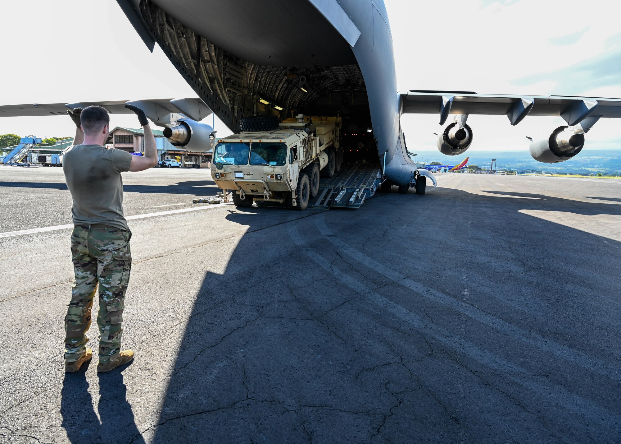 Senior Airman Andrew Girard, 535th Airlift Squadron C-17 Globemaster III loadmaster, directs a 25th Infantry Division light-medium tactical vehicle off of a C-17 Globemaster III at Hilo, Hawaii, Jan. 10, 2022. Equipment was transported to the Island of Hawaii for a gunnery sustainment exercise that will allow Soldiers to qualify on several weapon systems. (U.S. Air Force photo by Senior Airman Zoie Cox)