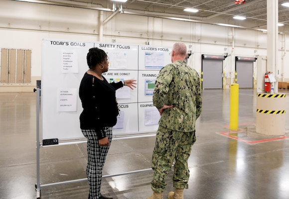 Photo shows woman speaking to man in uniform in front of a white board