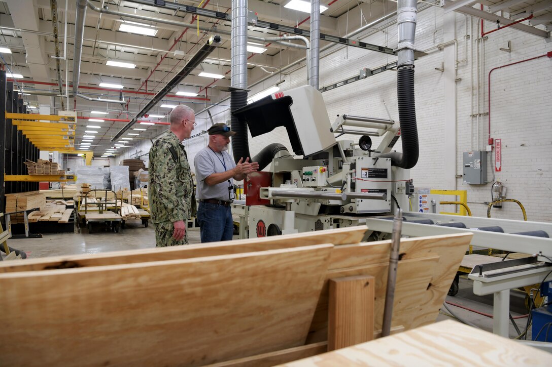 Photo shows two men speaking in front of large machinery