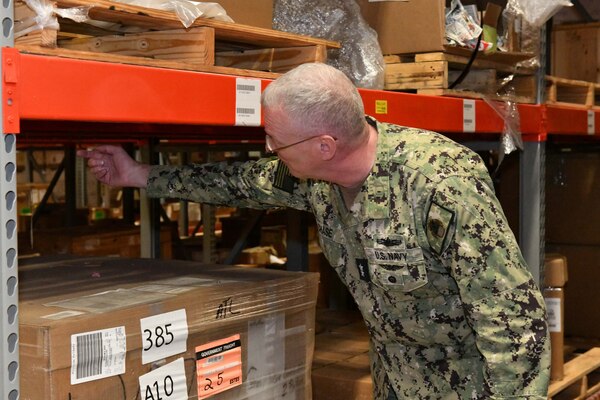 Photo shows man in uniform looking under shelves