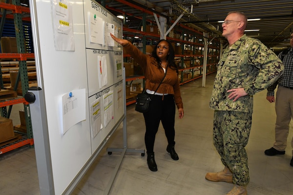 Photo shows woman speaking to man while looking at a white board