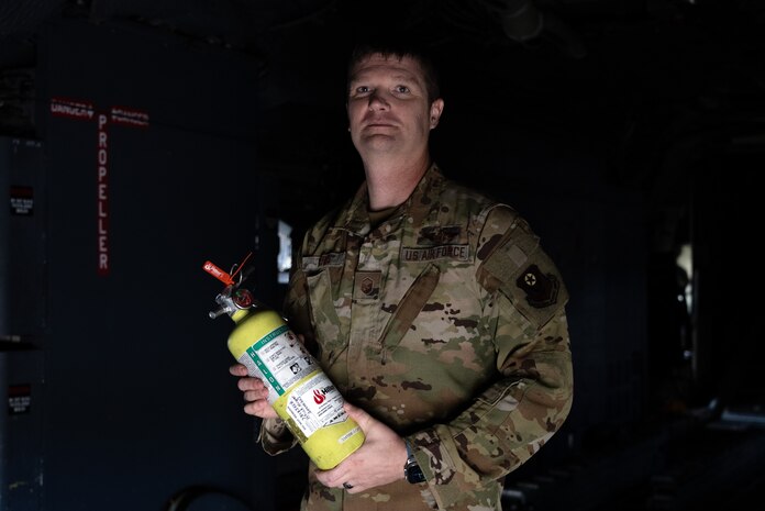 Man in Air Force uniform stands in the dark interior of a Combat Talon while holding a fire extinguisher.
