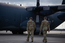 Two uniformed Airmen walk across pavement towards a Combat Talon aircraft in the background that greatly outsizes them.