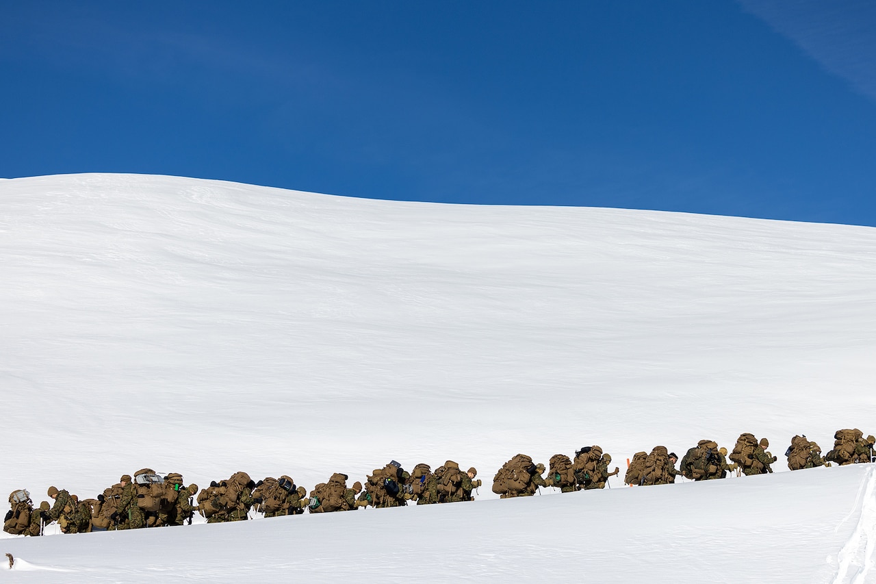 Marines are shown hiking up a snowy mountain.