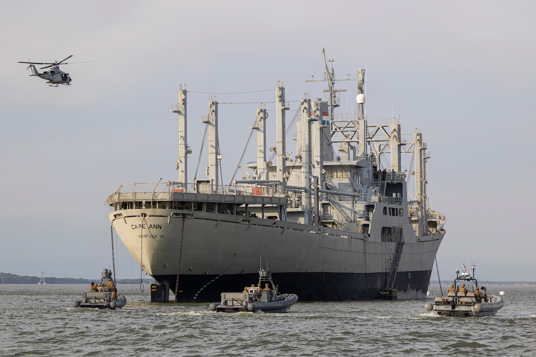 A large ship is escorted by three small boats and a helicopter.