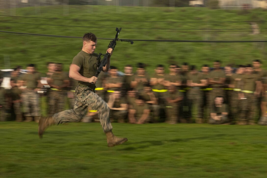 A Marine runs in front of a large group of Marines while carrying a machine gun.