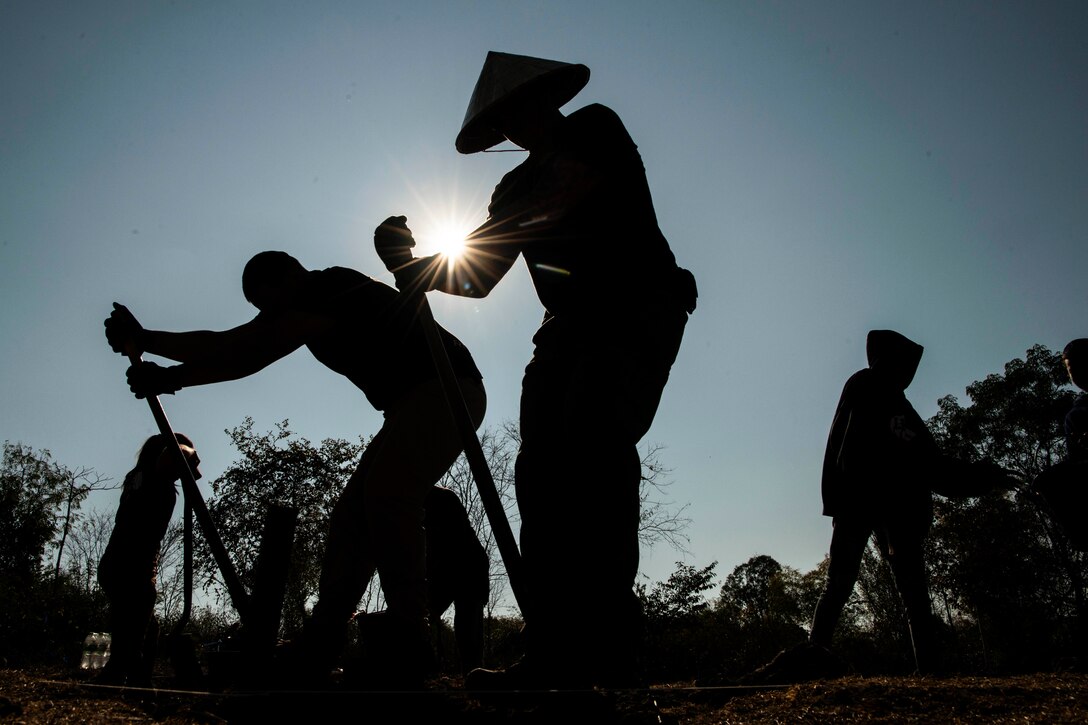 Personnel use shovels to dig in a field as shown in silhouette.