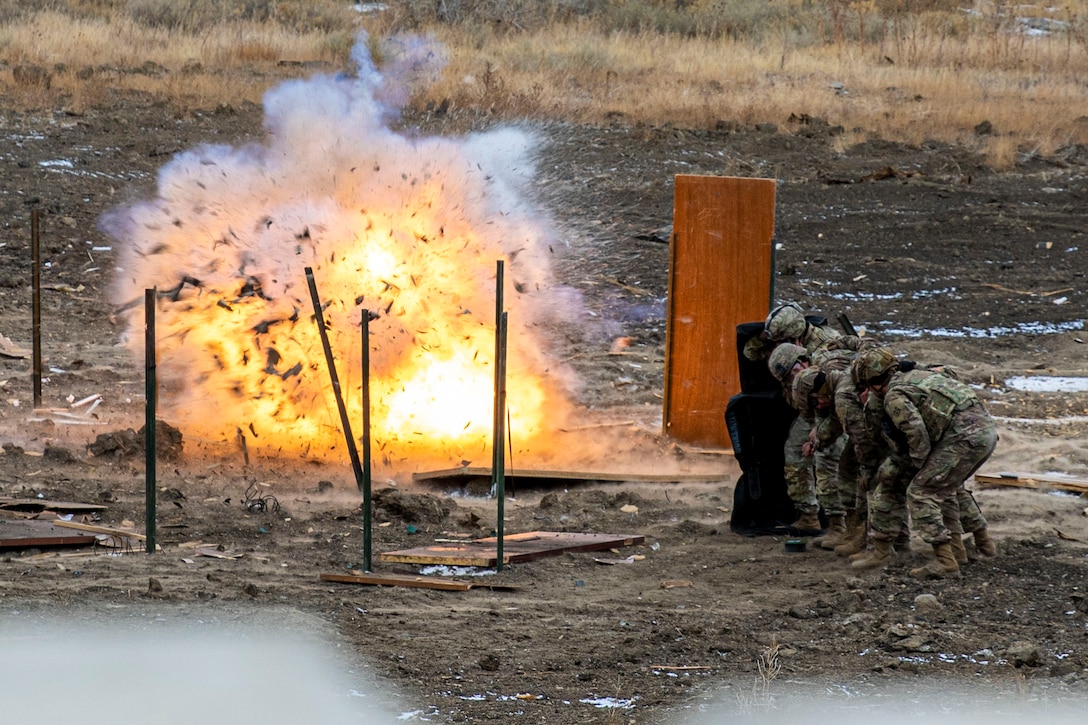 Soldiers stand behind a shield as an explosive detonates.