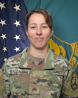 Women wearing U.S. Army uniform standing in front of two flags.