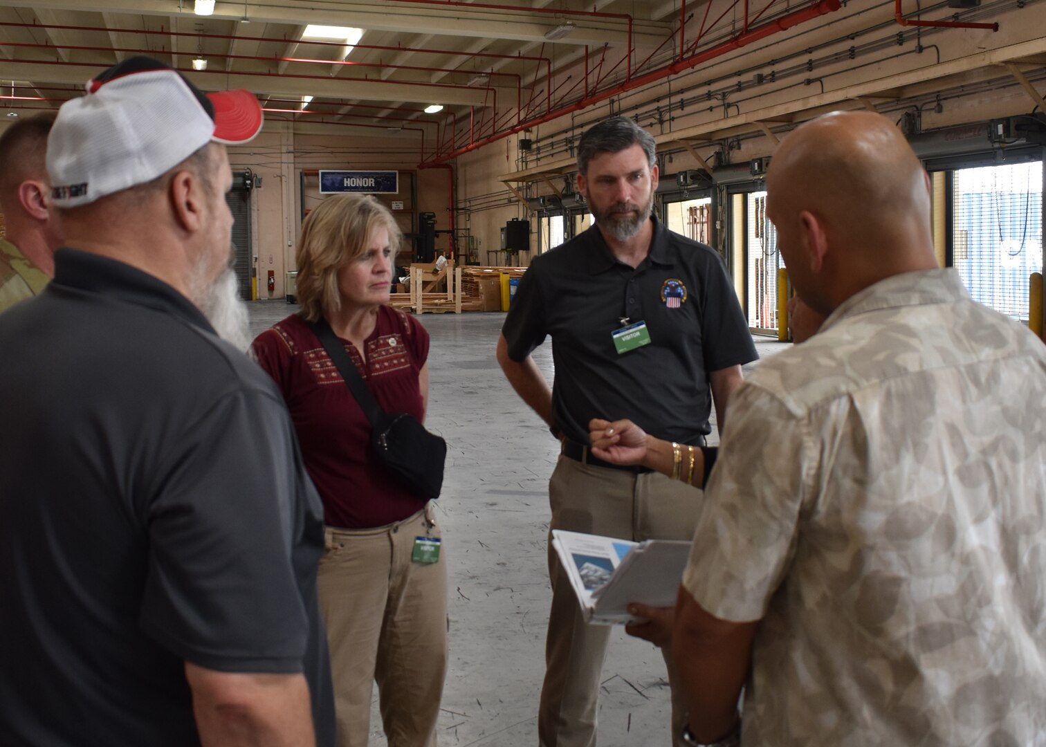 Three men and a woman stand in a warehouse talking.