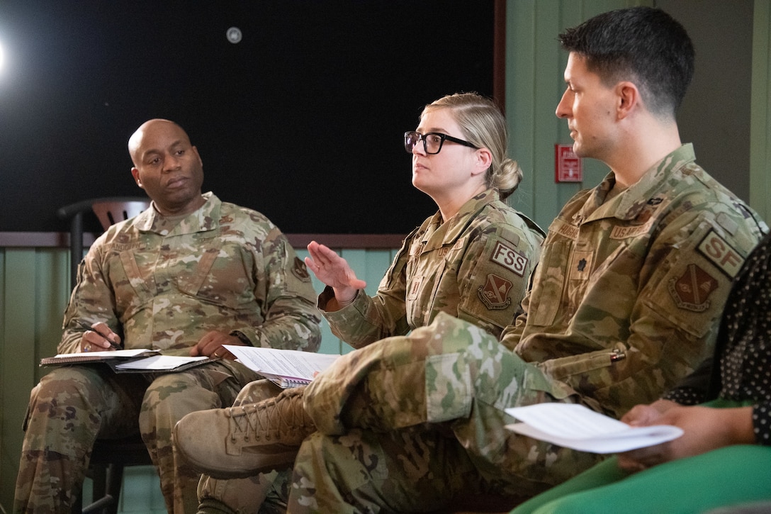 Two men and a woman sit in chairs on a stage.