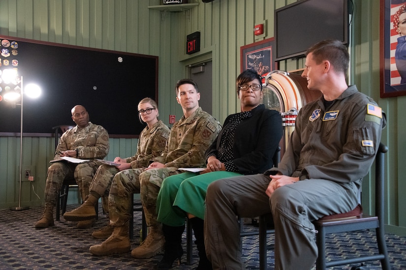 Five people sit in chairs on a stage.