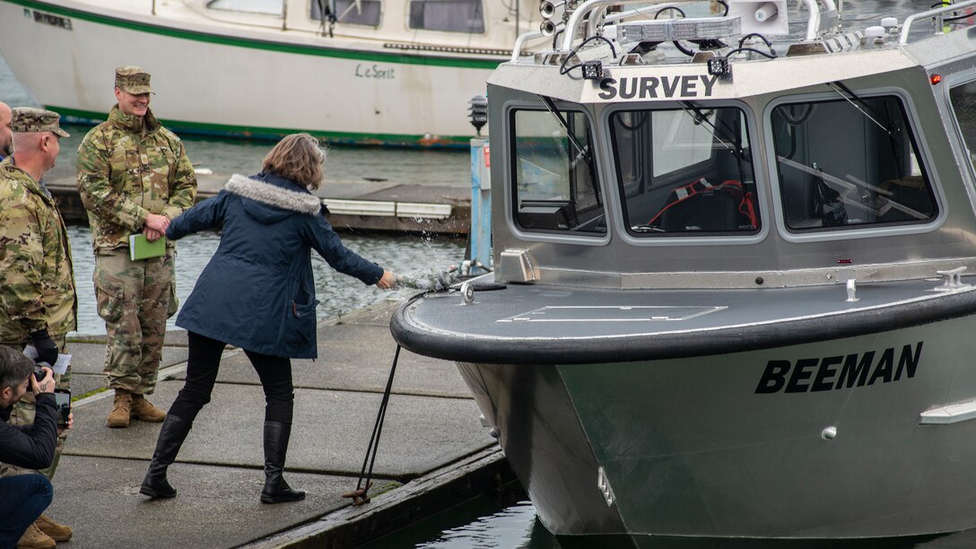 A woman breaks a bottle over the bow of a shiny, steel boat as part of a ship christening ceremony.