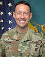 Man in U.S. Army uniform standing in front of two flags.