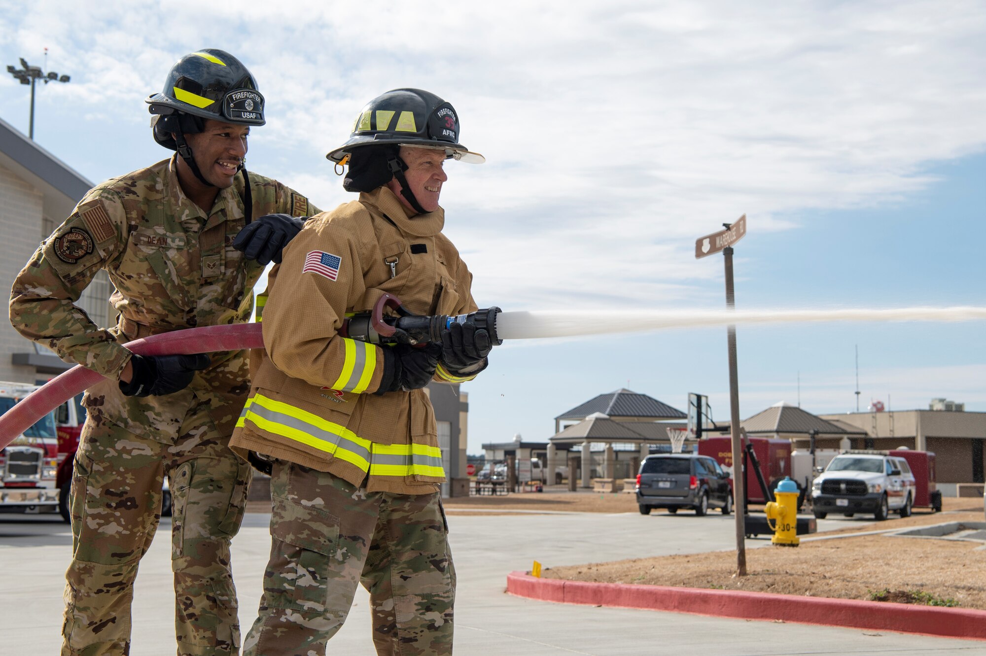 Two men in military uniforms use a fire hose during an event