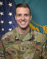 Man in U.S. Army uniform standing in front of two flags.