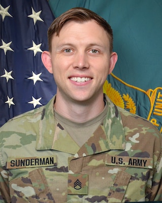 Man in U.S. Army uniform standing in front of two flags.