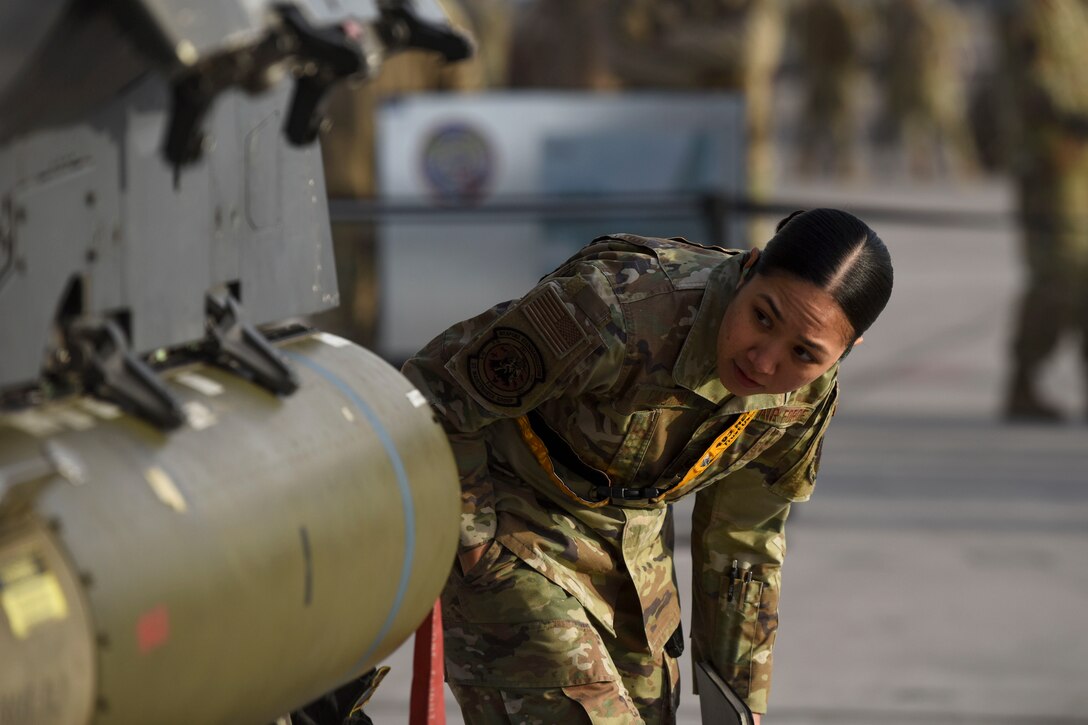 An airman leans over and looks at a weapon after loading.