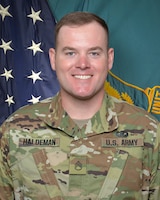 Man in U.S. Army uniform standing in front of two flags.