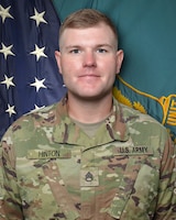 Man in U.S. Army uniform standing in front of two flags.