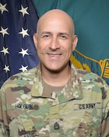 Man in U.S. Army uniform standing in front of two flags.