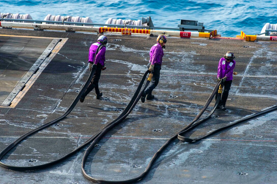 There sailors move a hose on the deck of a ship.