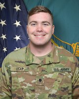 Man in U.S. Army uniform standing in front of two flags.