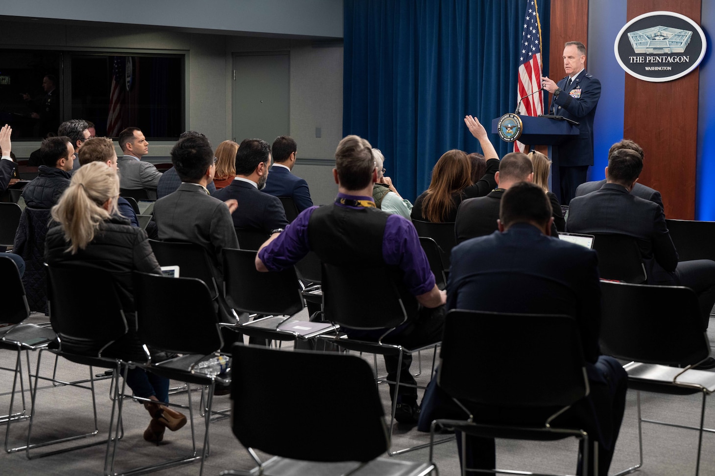 A man stands behind a lectern. Men and women sit in chairs in front of him.