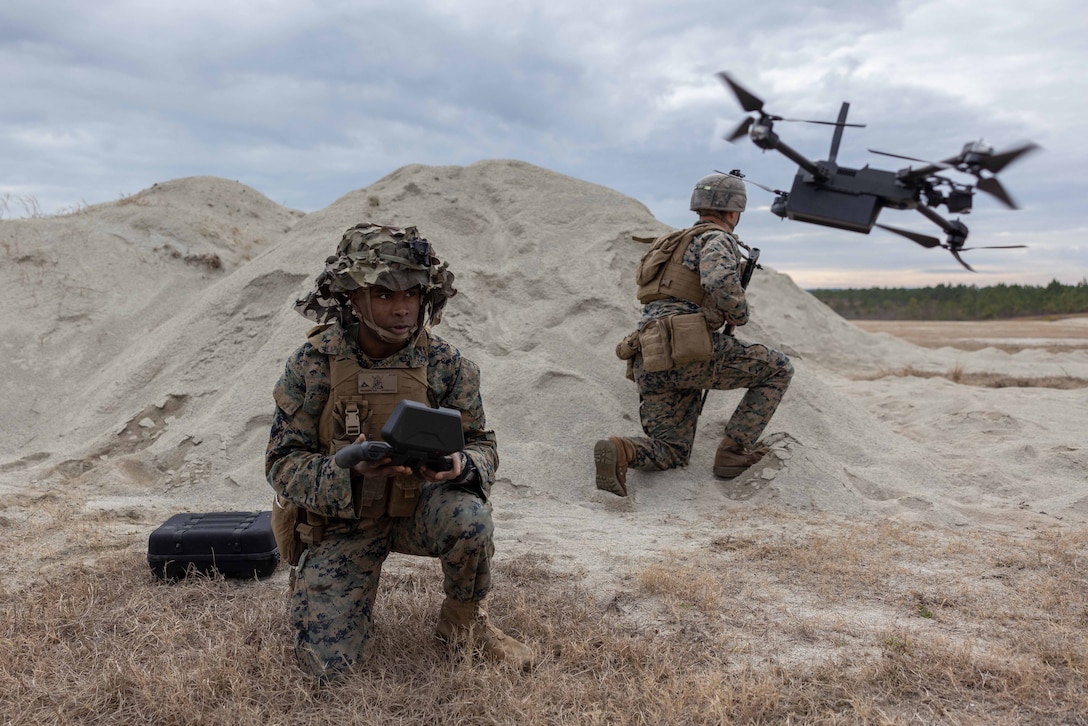 Marines kneel in a sandy mound as one operates a drone.