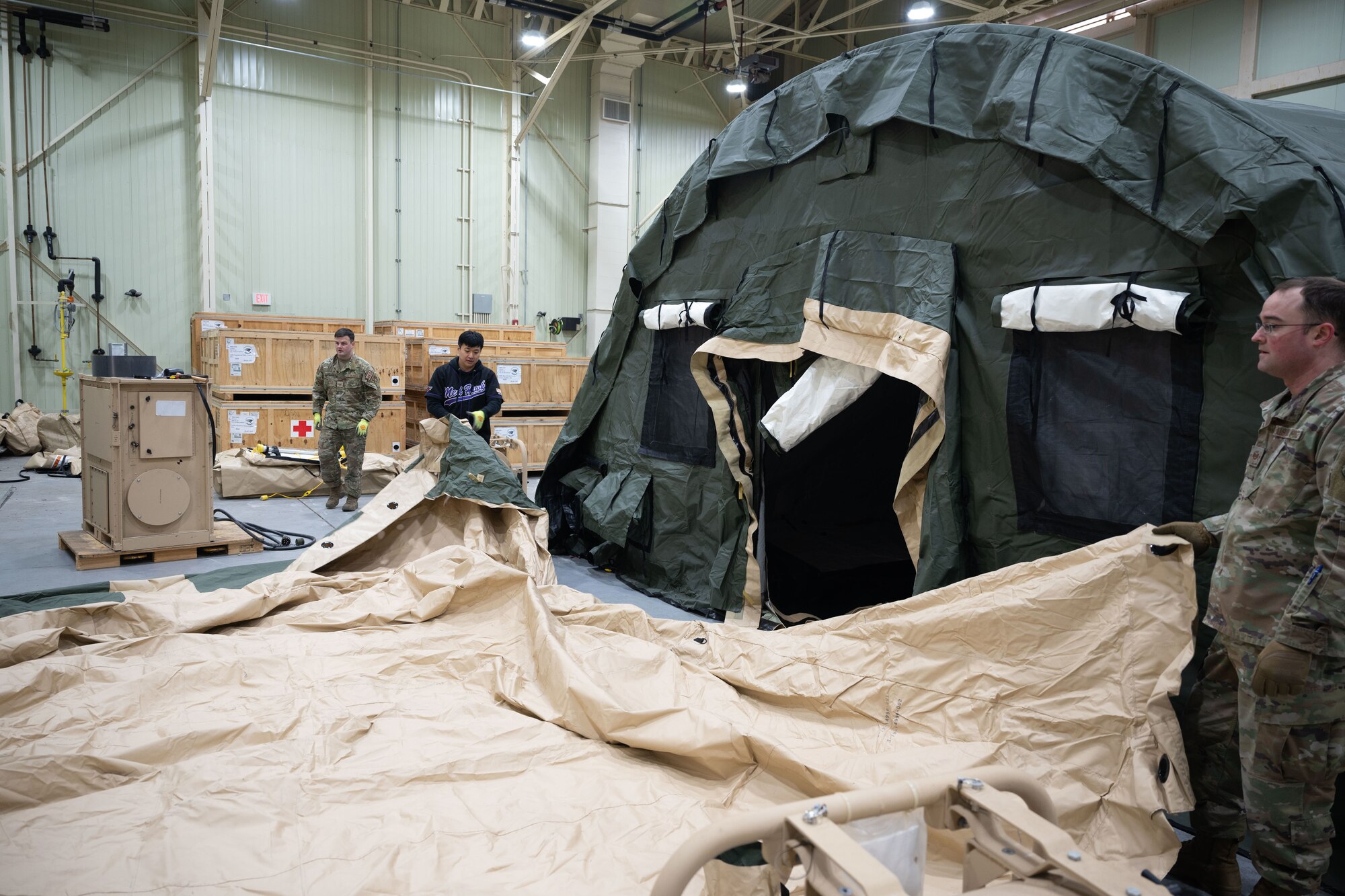 Tech. Sgt. Shane Borodycia (left), 8th Healthcare Operations Squadron (HCOS) section chief of contingency medical materiel, and Tech. Sgt. Tae Lee (middle), 8th HCOS section chief of supply operations, and Tech. Sgt. Jordan Williams, 354th Medical Group NCO in charge of medical materiel from Eielson Air Force Base, Alaska, unfold the top cover of the multi-functional entrance of a chemical protection system (CPS) at Kunsan Air Base, Republic of Korea, Jan. 20, 2023. Airmen from Eielson arrived to provide a week-long training for 8th HCOS Airmen on how to build a tent kit 2 CPS. (U.S. Air Force photo by Senior Airman Akeem K. Campbell)