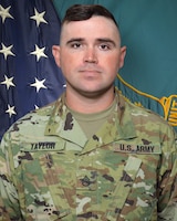 Man in U.S. Army uniform standing in front of two flags.