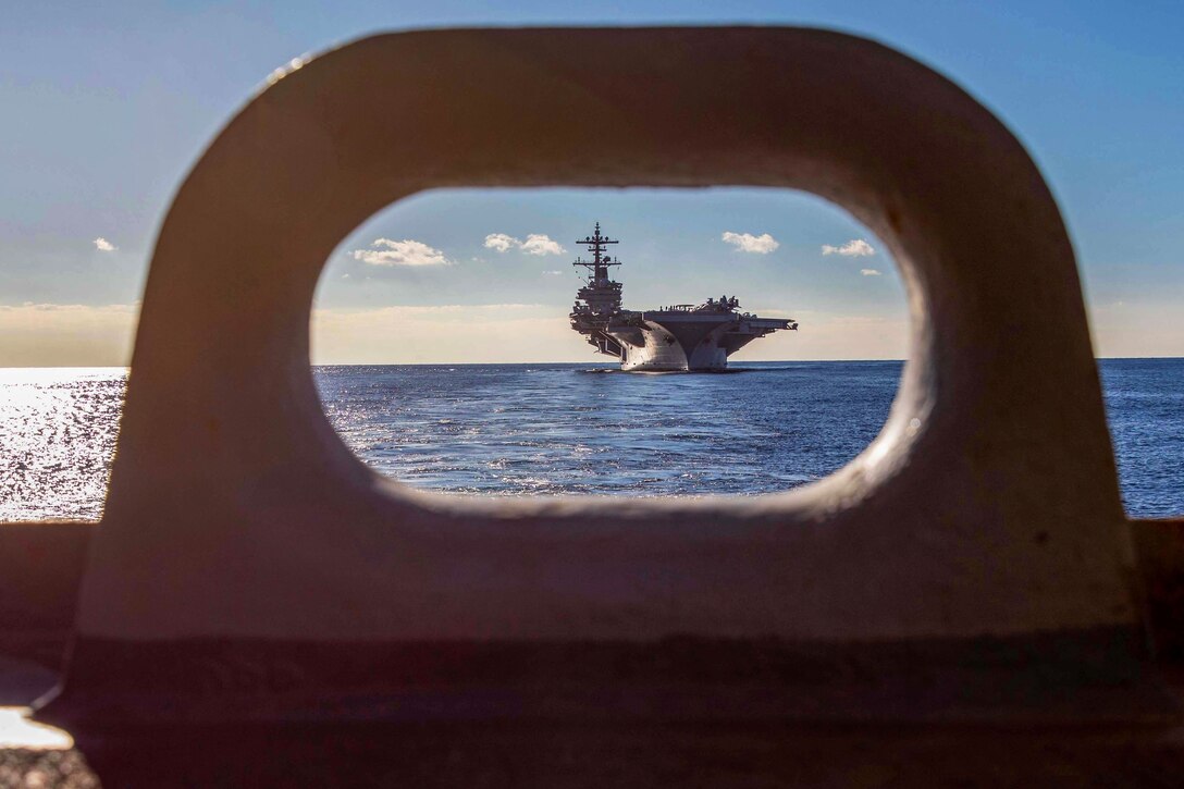 The USS George H.W. Bush is seen sailing through the opening of a structure.