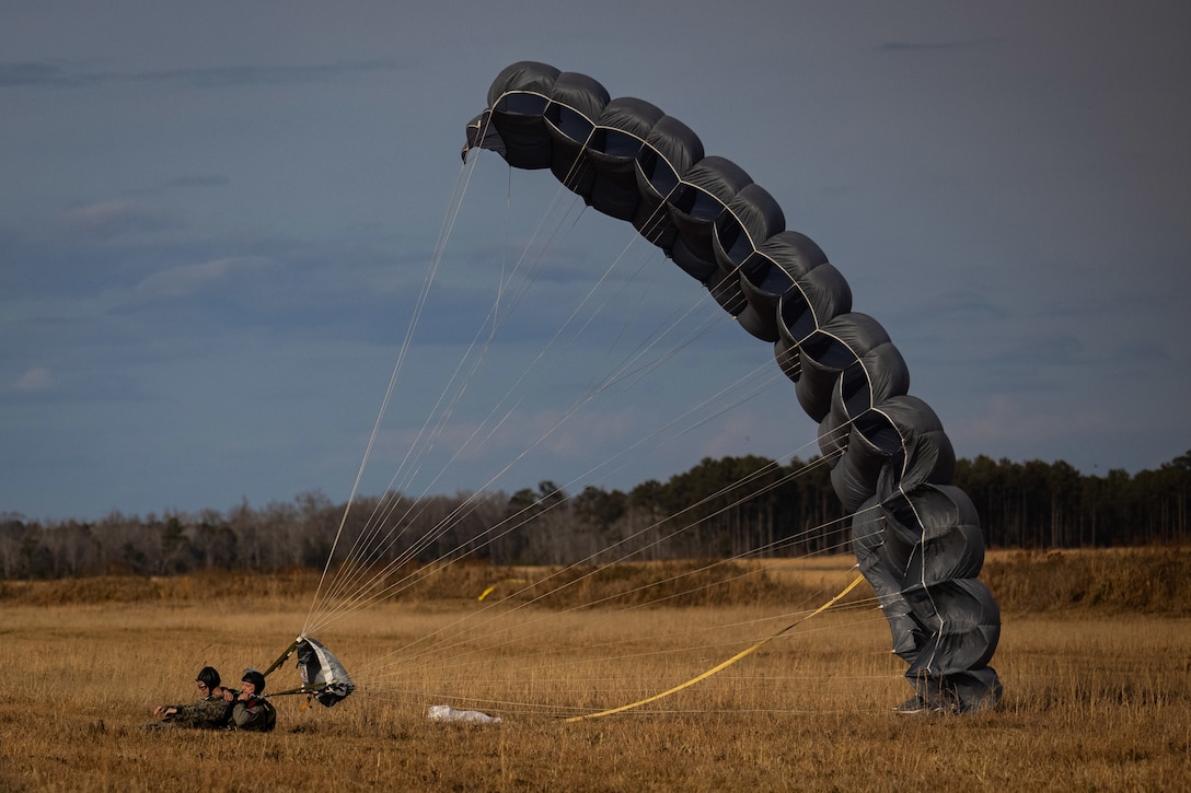 Marines lie in a field with a large parachute behind them.