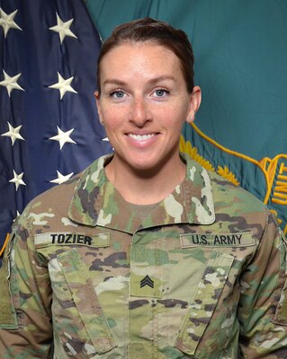Woman in U.S. Army uniform standing in front of two flags.