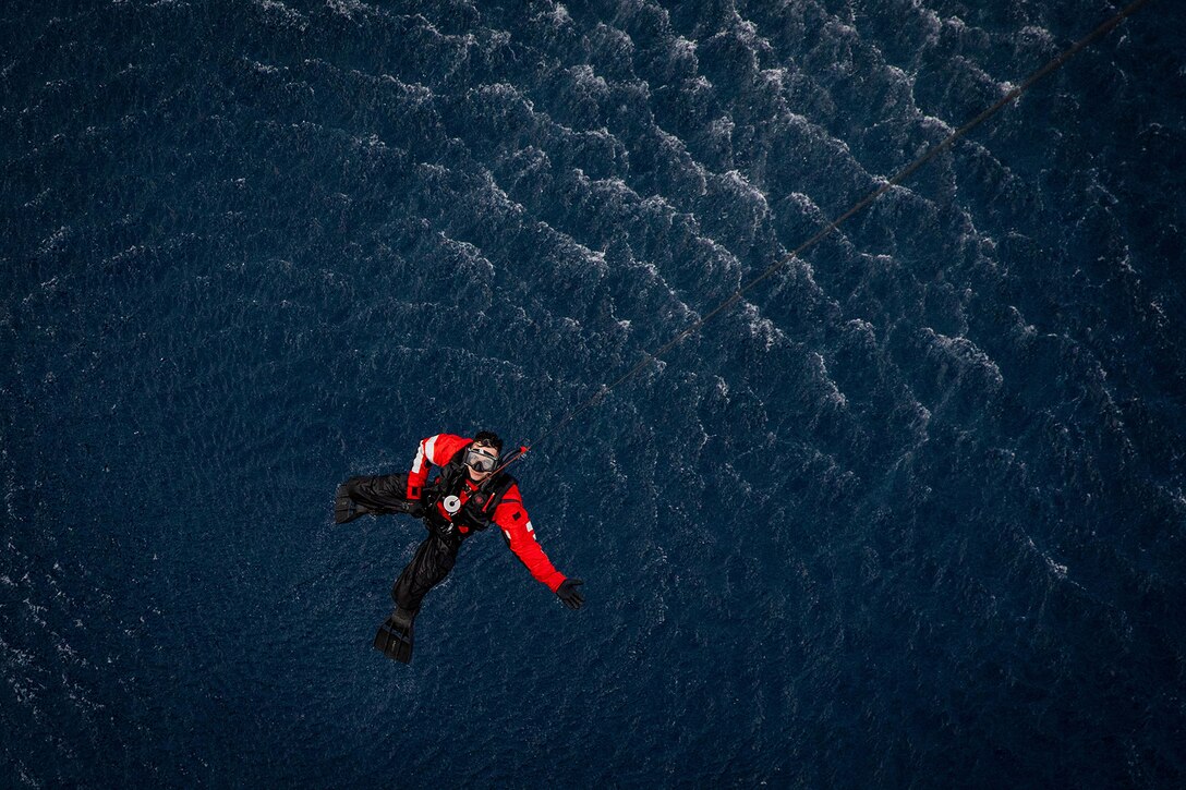 A service member is hoisted from the sea via helicopter.