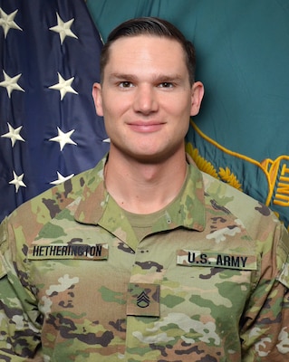 Man in U.S. Army uniform standing in front of two flags.