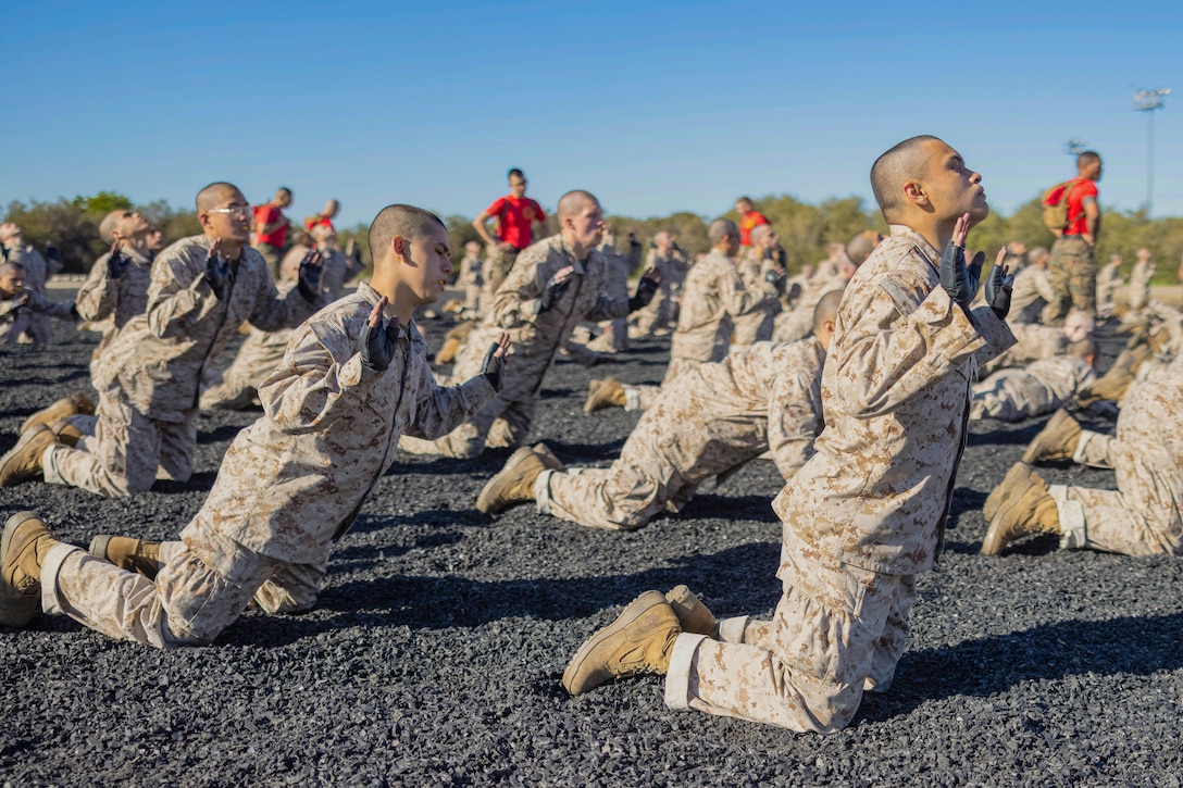 Marine Corps recruits on their knees fall forward on gravel.