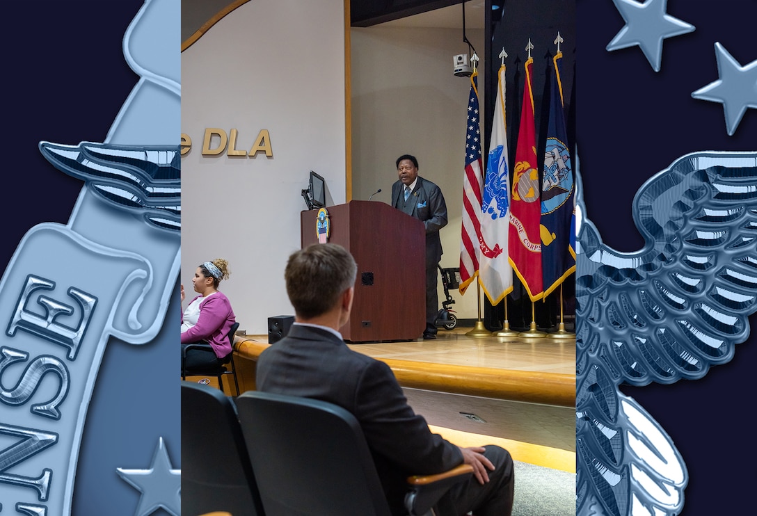 A dark skinned man delivers a speech on stage at a podium in an auditorium.