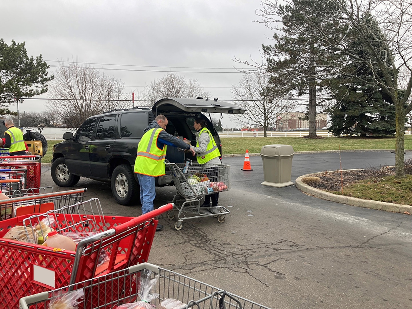 A man and a woman in a a yellow reflective vests load a car trunk with food outside in a parking lot.